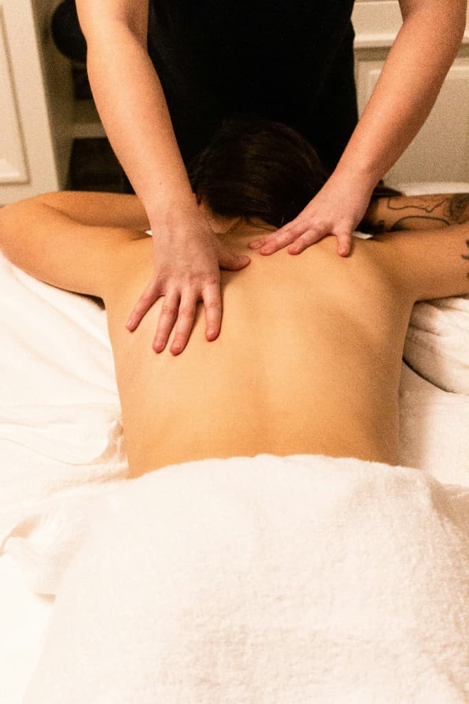 Massage therapist using both hands to relieve tension through a client's shoulders and upper back